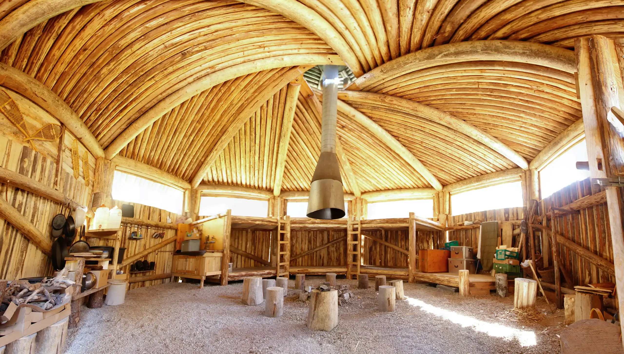 Innenraum der Holzhütte im Camp Yukon mit Runddach, Feuerstelle und Kochbereich aus Naturmaterial
